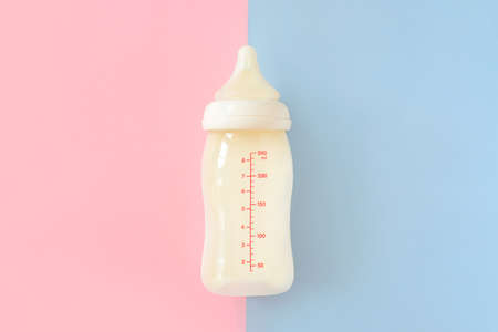 Bottle of milk for newborn baby over pink and blue pastel colors background. Maternity and baby care concept. Top view.の写真素材