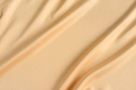 Close up of ripples in gold colored silk fabric. Satin textile background. Free copy space.の写真素材