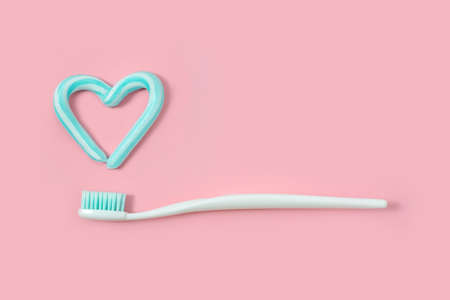 Toothbrushes and turquoise color toothpaste in shape of heart on pink background. Dental and healthcare concept.の写真素材