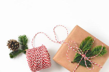 Christmas gift wrapped in craft brown paper and decorated with fir-tree branches isolated on whote background. New year gift giving concept. Free copy space.の写真素材