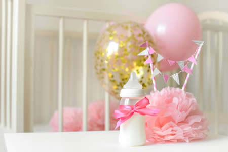 Baby bottles with breast milk with various festive paper decor and balloons in front of baby bedroom. It's a girl or baby birthday celebration concept. Baby shower concept.の写真素材