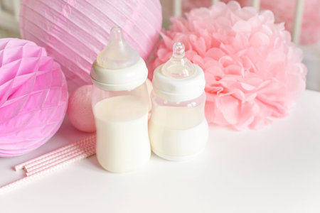 Baby bottles with breast milk with various festive paper decor and balloons in front of baby bedroom. It's a girl or baby birthday celebration concept. Baby shower concept.の写真素材