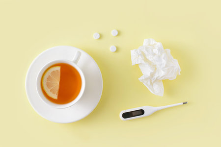 Pills, napkins for the nose, thermometer and cup of tea on yellow background. Cold and flu treatment...