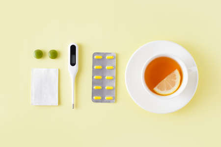 Pills, thermometer and cup of tea on yellow background. Cold and flu treatment set. Flat lay, top view. Free copy space.の写真素材
