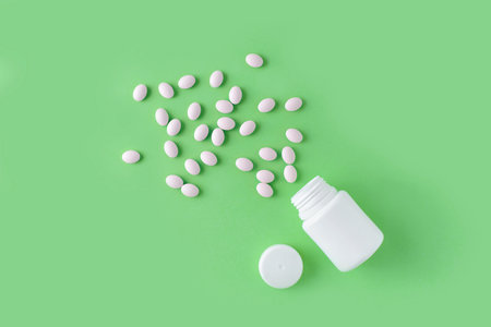 White pills and bottle on green background. Medical pharmacy concept. Probiotics benefits.