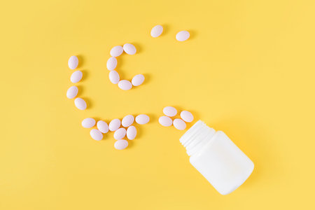 Vitamin c pills dropped from bottle on yellow background. Flat lay, top view, free copy space.