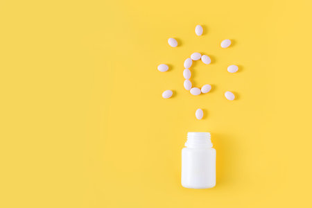 Vitamin c pills dropped from bottle on yellow background. Flat lay, top view. Free copy space.