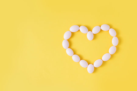 Pills in shape of heart on yellow background. Flat lay, top view. Free copy space.の写真素材