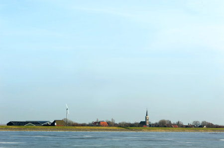 Ice on water in front of distant city in Netherlands. View on old church, houses and windmill. Free...