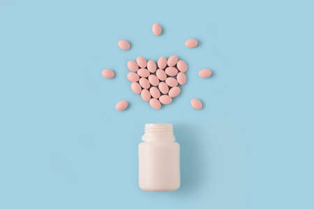 Pink pills in shape of heart and bottle on blue background. Medical pharmacy concept. Healthy life style.の写真素材