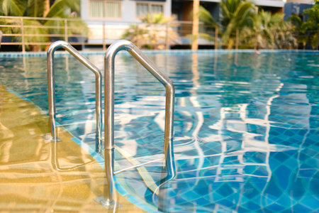 Swimming pool with grab bars ladder and stairs. Green palm trees outside.