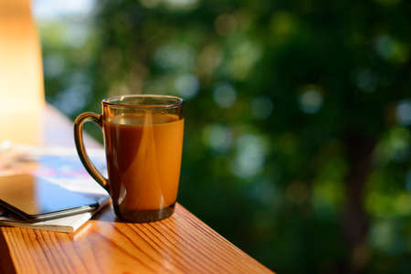 Cup of coffee and cellphone on the windowsill over blurred forest background at sunny summer day. Free copy space.の写真素材