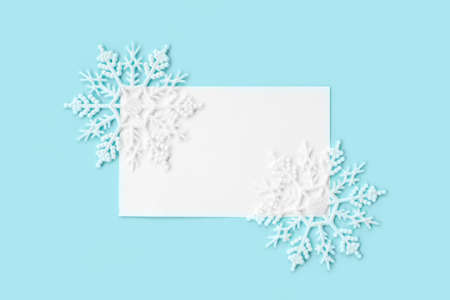 White paper card decorated with snowflakes on light blue background. New Year, Christmas and winter concept. Flat lay, top view, free copy space.の写真素材