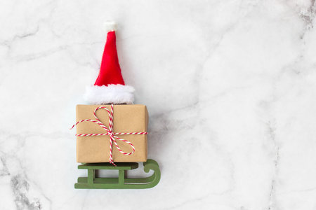 Christmas gift wrapped in brown craft paper and red hat on wooden sleigh Christmas toys on gray...