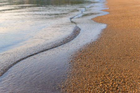 Sea wave and sand seashore. Golden sun light over the sea ocean waves. MIrror reflection on water surface. Macro close up.の写真素材