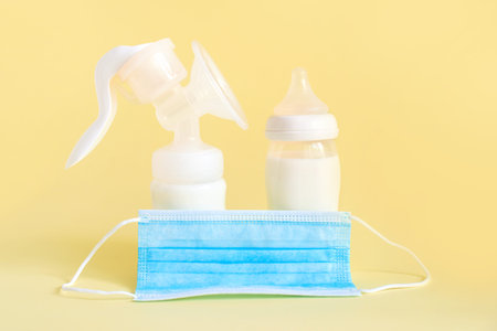 Set of breast pump and bottles with breast milk for baby and medical mask on yellow background. Maternity and baby care concept.の写真素材