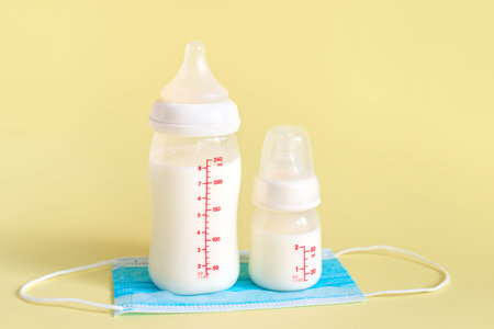 Set of bottles with breast milk for baby and medical mask on yellow background. Maternity and baby care concept.の写真素材