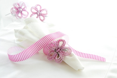 White linen serviette with pink beaded napkin ring on a white background with space for textの写真素材
