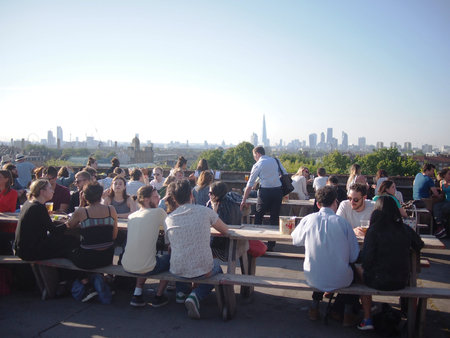 Peckham, London, UK - June 12, 2015: Young adults eating and drinking on a rooftop bar during a hot...