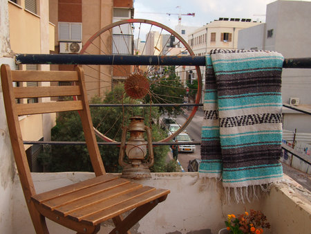A wooden chair and a rug hanging on a sunny balcony in a Tel Aviv apartmentの写真素材