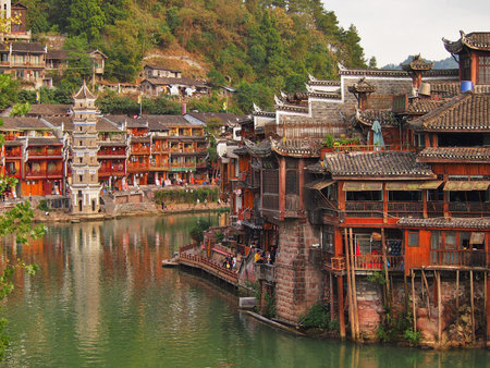 Fenghuang, China - 17 October, 2016: Tradtional oriental architecture on display in the old town of Fenghuang, Hunan. The colourful green river contrasts with the rickety red homes hanging over the water.のeditorial素材