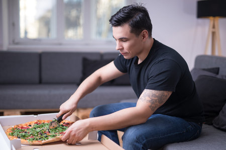 Young handsome man eating pizzas in his apartment aloneの写真素材