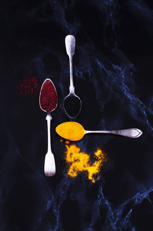 Spices on silver spoons on a dark background