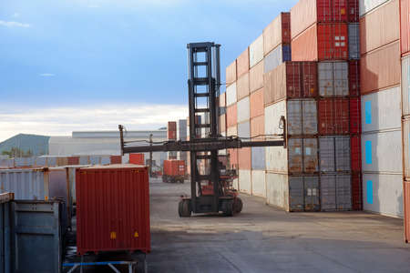 Forklift truck handling cargo container boxes in logistic delivery yard with stacks of cargo containers in background.の写真素材
