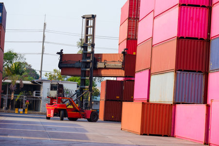 Forklifts handle shipping boxes in a shipping yard with a stack of containers behind them.