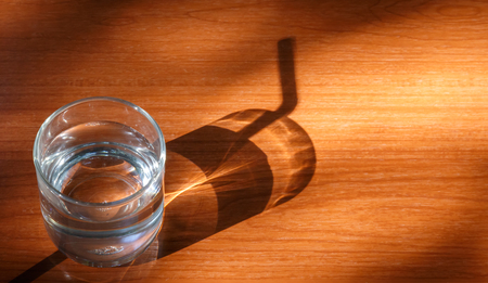Glass of water on dark tile floor with light and shadow, Top view with space for text.の写真素材