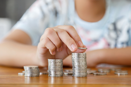 A girl putting coins to rising stack of coins on wooden table.の写真素材