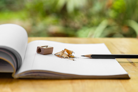 Open note book with pencil, sharpener and shavings on wooden and green background.の写真素材
