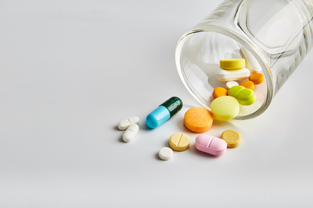Various pills poured out of the glass on white backgroundの写真素材
