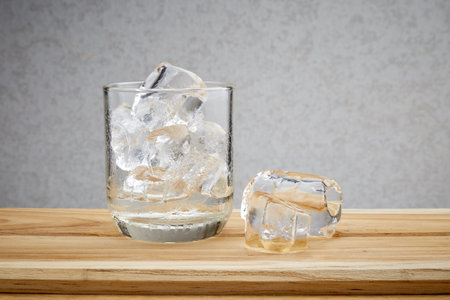 Glass with ice cubes on wooden against grey wall background