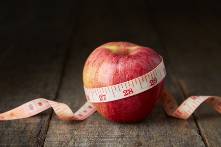Red apple with measuring tape on old wooden board, concept of weight loss, diet, nutritionの写真素材