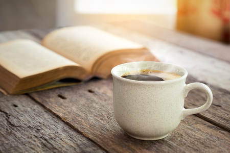 Coffee cup and open book on old wooden table with sunlight from window curtain bavkgroundの写真素材
