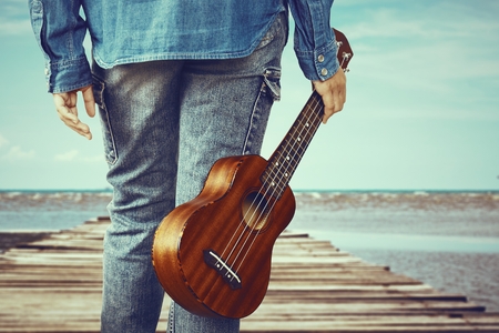 Close up of  Hipster girl holding ukulele guitar stand alone on wooden bridge over the sea, vintage tone effectの写真素材
