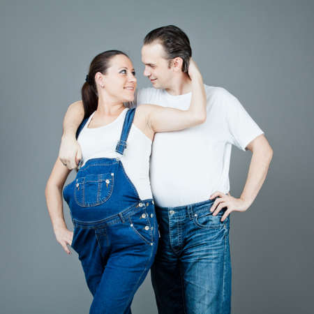 A man and a pregnant woman, the couple posing on a gray backgroundの写真素材