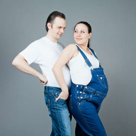 A man and a pregnant woman, the couple posing on a gray background の写真素材
