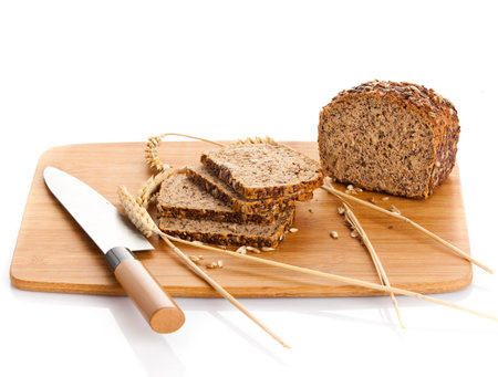 Fresh bread being sliced on a wooden cutting board with a bread knife. Isolated over white