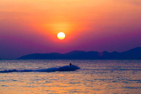 the jetski above the water at sunset.  Silhouette of people on a jet ski running pass the romantic sunset in the sea.の写真素材