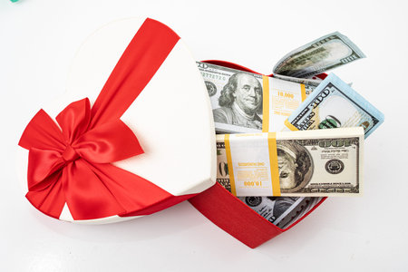 Bundle of dollars in heart gift box with bow isolated on white