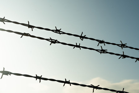 Barbed wire on fence with blue sky to feel worrying