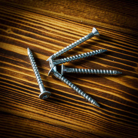 Closeup shot of a row of screws laid on a wooden tableの写真素材