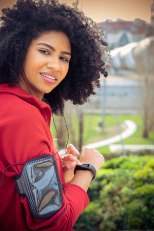 Beautiful athlete woman preparing to run with earphones , smart watch and mobile app in the park