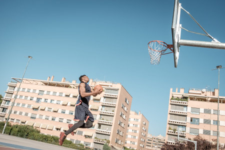 One afroamerican young man is playing basketball in a park in Madrid during summer at midday. He is...