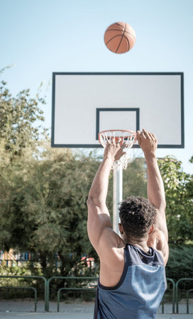 Close-up from the back of one afroamerican young man is playing basketball in a park in Madrid...