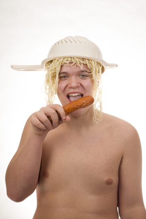 A young, fat, cheerful, smiling boy eating spaghetti and having a colander on his head. Plump body without clothing. White background. Portrait photo.の写真素材