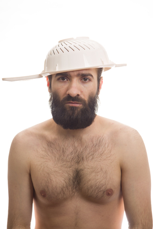 Bearded, funny, young man with a colander on his head. White background. Body without clothing. Portrait photo. Caucasian guy.の写真素材