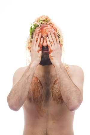 Bearded, funny, young man with spaghetti on his head. Sauce. White background. Dirty, body without clothing. Portrait photo. Caucasian guy.の写真素材